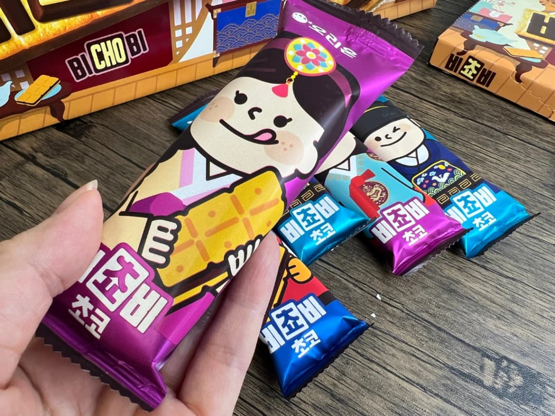 コストコの韓国チョコ菓子「ビチョビ」の個包装パッケージ。韓国風の衣装を着たキャラクターが描かれた紫色の袋と、色違いの個包装を紹介