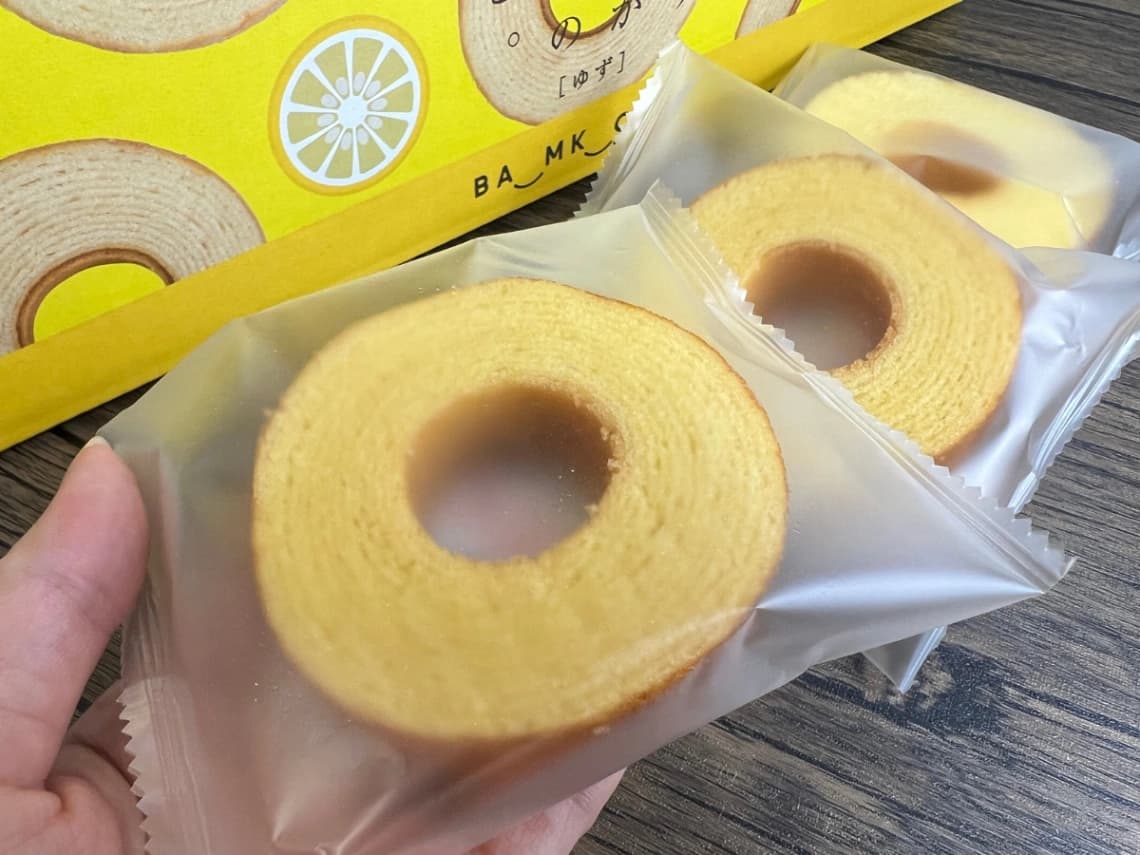コストコ「おとなのばうむ。ゆず」の個包装パッケージ。手に持ったバウムクーヘンと黄色い外箱を紹介