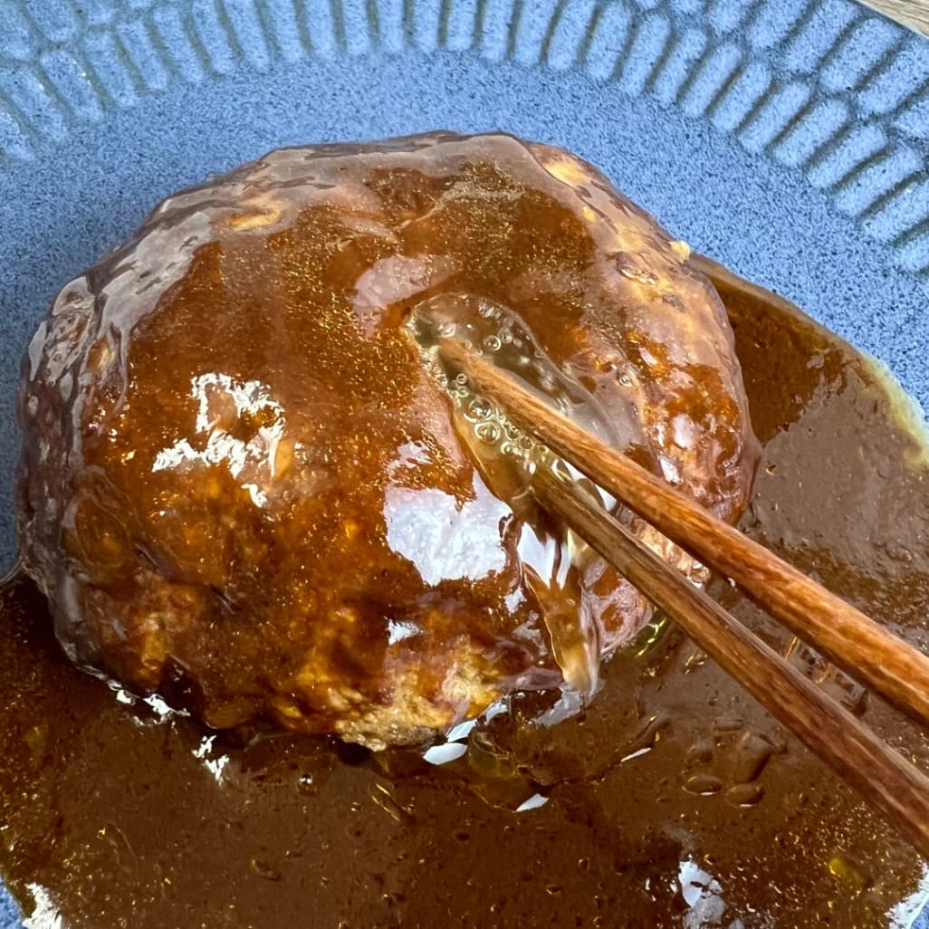 コストコのデミグラスハンバーグステーキを箸で押す様子・表面ににじむ肉汁と濃厚ソース