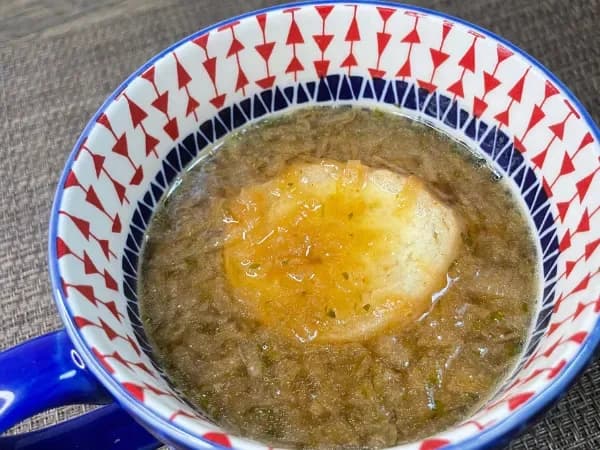 マグカップに注いだオニオングラタンスープ。表面にバゲットとチーズが浮かぶ調理途中