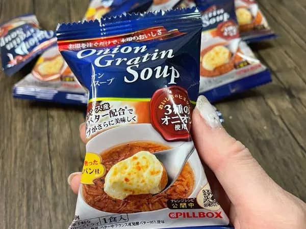 「PILLBOX オニオングラタンスープ」個包装を手に持ったサイズ感。背景に小袋が並ぶ