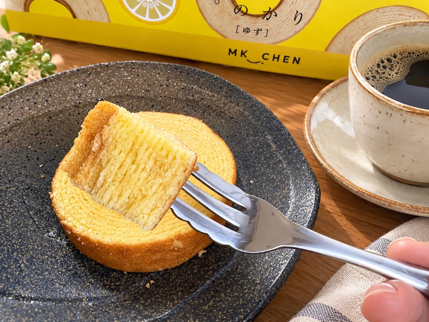 コストコ「千年屋 おとなのばうむ。ゆず」の実食レビュー。フォークで持ち上げたバウムクーヘンの断面から、しっとりとした生地の層がわかる。コーヒーと一緒に盛り付けた様子。